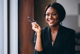 Uma mulher negra de negócios sorrindo e segurando seus óculos.